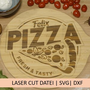 May include: A wooden pizza cutting board with a laser-engraved design that says "Felix Pizza Fresh & Tasty". The board has a handle and is surrounded by ingredients like mushrooms, tomatoes, and basil.