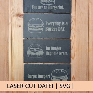 Puede incluir: Cuatro posavasos de pizarra negra con ilustraciones de hamburguesas blancas y refranes divertidos sobre el tema de las hamburguesas. Los refranes son "You are so Burgerful", "Everyday is a Burger DAY", "Im Burger liegt die Kraft", y "Carpe Burger!"