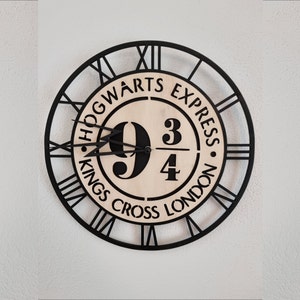 Könnte beinhalten: Eine runde Wanduhr mit schwarzem Rahmen und römischen Ziffern. Das Zifferblatt zeigt den Text "Hogwarts Express" und "Kings Cross London" um ein zentrales Design mit den Zahlen "9 3/4". Die Uhrzeiger sind schwarz.