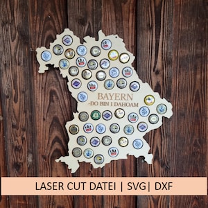 Puede incluir: Un recorte de madera del estado de Baviera, Alemania, con el texto "BAYERN -DO BIN I DAHOAM" y un diseño para sujetar tapones de botellas.
