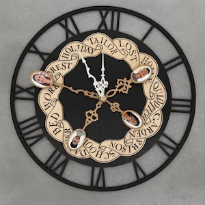 Könnte beinhalten: Eine schwarze und beige Wanduhr mit römischen Ziffern und einem dekorativen Innenkreis. Der Innenkreis zeigt vier Fotorahmen und die Wörter "Holiday", "Tailor", "Lost", "Home", "Quidditch", "Garden", "Prison", "School", "Bed", "Work" und "Forest".