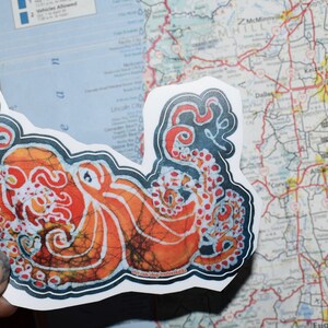 May include: A sticker featuring a colorful octopus with a batik pattern. The octopus is orange, red, and white with black outlines. The sticker is on a white background.