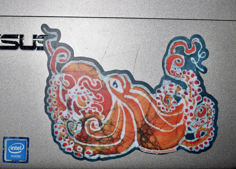 May include: A colorful sticker of an octopus with a batik-style design in shades of orange, red, and white. The octopus is curled up with its tentacles intertwined.