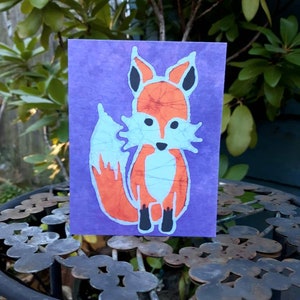 May include: A purple card with a batik fox design. The fox is orange and blue with black ears and feet.