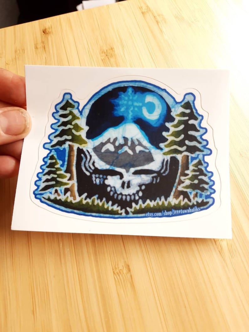 May include: A blue and white sticker featuring a mountain scene with a crescent moon. The mountain is surrounded by two pine trees. The sticker has a blue border and the text "etsy.com/shop/treetownbatiks" at the bottom.