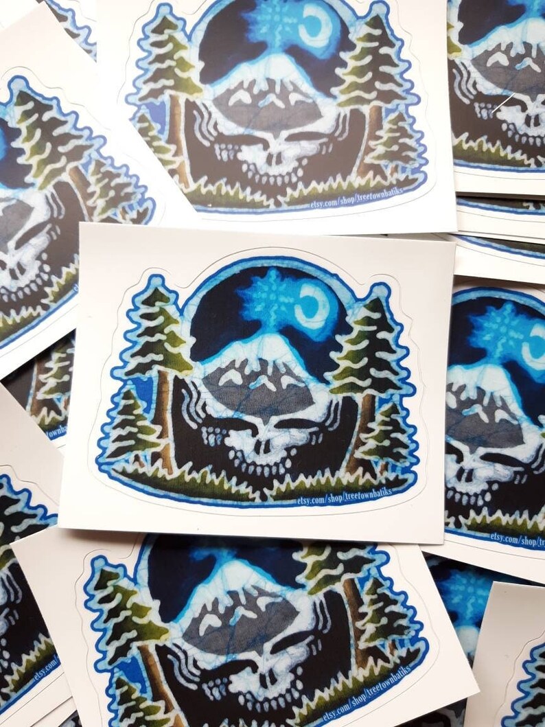 May include: A set of colourful stickers featuring a psychedelic skull design with mountains, trees, and a crescent moon. The stickers are printed on white paper and have a glossy finish.