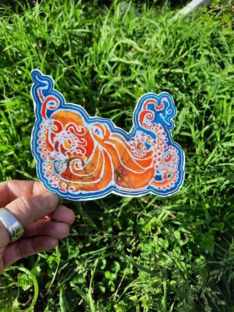 May include: A colorful sticker featuring an orange and blue octopus with white and red details. The octopus is drawn in a batik style with a swirling pattern.