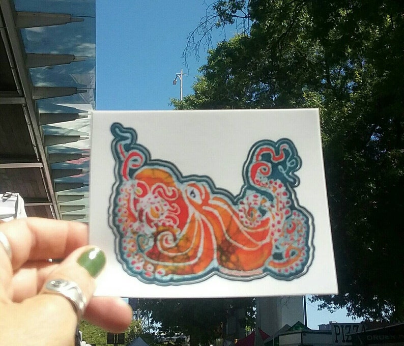 May include: A white sticker with a colorful octopus illustration. The octopus is orange, red, and blue with a batik pattern. The octopus has eight tentacles.