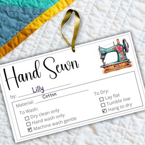 May include: A white tag with the text "Hand Sewn" in cursive script. The tag also includes the text "by: Lilly Cotton" and a list of care instructions for the item. The tag features a cartoon illustration of a sewing machine with a floral design.