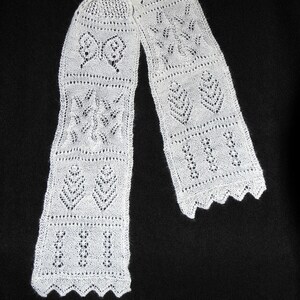 May include: White crocheted scarf with a delicate lace pattern. The scarf features a repeating design of hearts and butterflies.