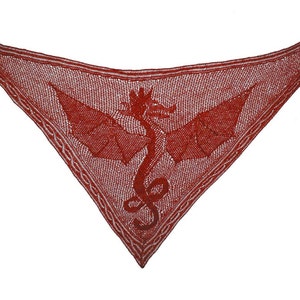 May include: A red knitted shawl featuring a dragon design in the centre. The dragon is outlined in white and has its wings spread out.