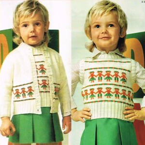 May include: Two children wearing white knitted sweaters with a red, green, and orange pattern of stick figures holding hands. The sweaters are worn over green skirts.