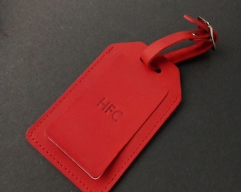 May include: Red leather luggage tag with a stitched edge and a silver metal loop. The tag has the initials "HFC" embossed on the front.