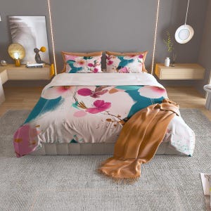 May include: A white and pink floral duvet cover with a teal and white abstract design. The duvet cover is on a bed with a brown throw blanket.