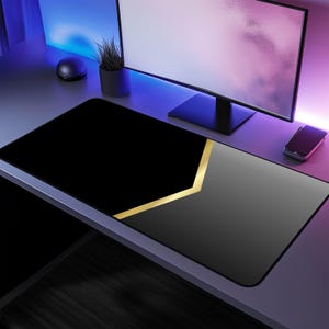 May include: A black and gray gaming mouse pad with a gold geometric design. The mouse pad is on a desk with a computer monitor and a plant.