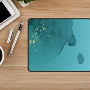 May include: A teal blue mouse pad with a white and gold abstract design. The design features a large, flowing shape with gold flecks throughout.