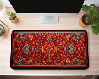 May include: A red, black, and gold patterned desk mat with a floral design. The mat is on a wooden desk with a computer monitor and a potted plant.