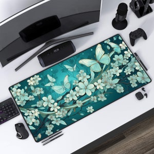 May include: A teal blue mousepad with a floral design featuring delicate white flowers and butterflies. The butterflies are a light blue color with gold accents.