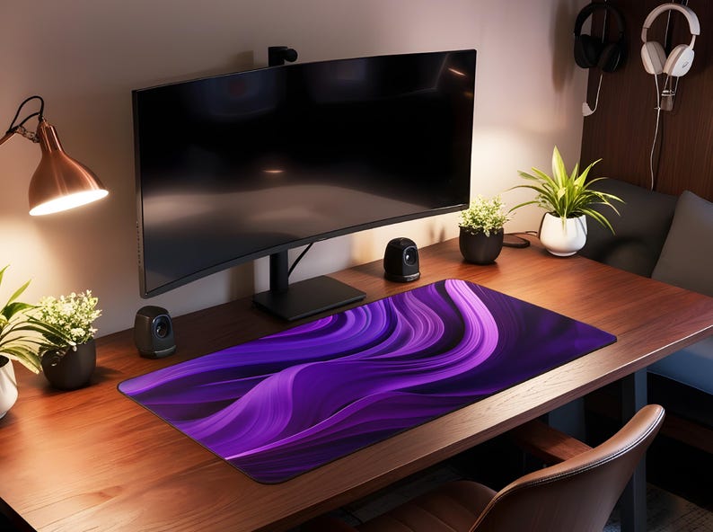 May include: A purple and black abstract design mousepad with a curved design. The mousepad is on a wooden desk with a computer monitor, a lamp, and plants.