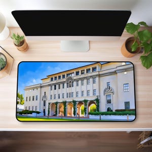 May include: Rectangular mousepad featuring a detailed image of a large, light-colored building with multiple windows and arched entryways. The building is set against a blue sky, with green foliage and a black border.
