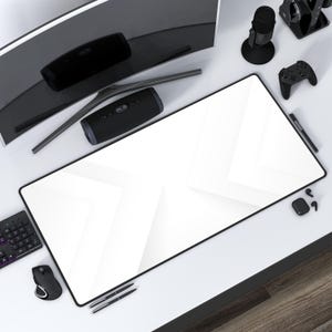May include: A white desk mat with a geometric pattern. The mat is on a white desk with a black computer monitor, a black speaker, a black microphone, a black gaming controller, a black keyboard, a black mouse, and a black pen.