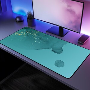 May include: A teal and gold abstract design desk mat with a smooth surface. The mat is on a desk with a computer monitor and a plant.