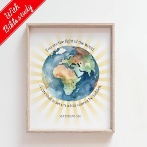 Op de afbeelding: Ingelijste print met een aquarel illustratie van de aarde, in tinten blauw, groen en bruin. De tekst luidt "Jij bent het licht van de wereld" en "Een stad die op een berg ligt, kan niet verborgen zijn." De bijbelverwijzing Mattheüs 5:14 is ook opgenomen.