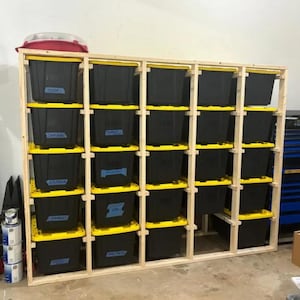May include: A wooden storage shelf unit with multiple black storage bins with yellow lids. The bins are labeled with blue tape.