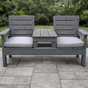 May include: A white ceramic mug with a black handle and the text "But First, Coffee" in a bold, black font. The mug is set against a blurred background, suggesting a cozy setting.