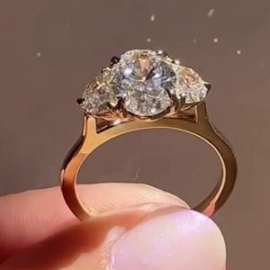 Könnte beinhalten: Ein goldener Ring mit einem großen ovalen Diamanten und zwei kleineren birnenförmigen Diamanten an jeder Seite.