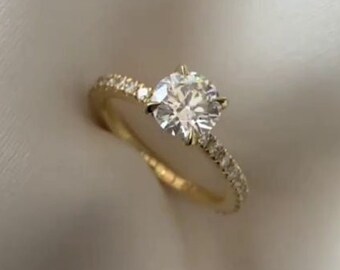 Op de afbeelding: Een gouden verlovingsring met een ronde, heldere middelste steen en een band met kleinere diamanten.