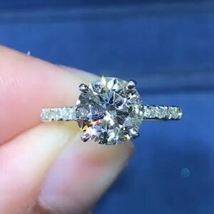 Op de afbeelding: Een zilveren verlovingsring met een grote, ronde, heldere diamant in het midden en een band met kleinere diamanten.