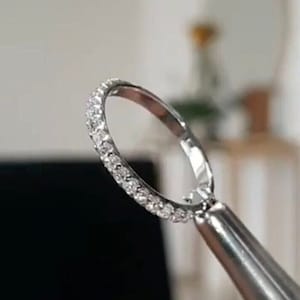 Könnte beinhalten: Ein silberner Bandring mit einer Reihe kleiner, klarer Diamanten, die um die gesamte Band gefasst sind.