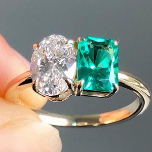 May include: A gold ring with a large oval-shaped diamond and a square emerald gemstone.