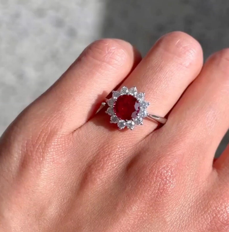 May include: A silver ring featuring a large red ruby gemstone encircled by a halo of smaller white gemstones.
