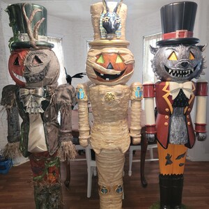May include: Three Halloween-themed nutcrackers. The first is a scarecrow with a pumpkin head, the second is a mummy with a jack-o'-lantern face, and the third is a werewolf with a top hat. Each figure has a unique design and color scheme.