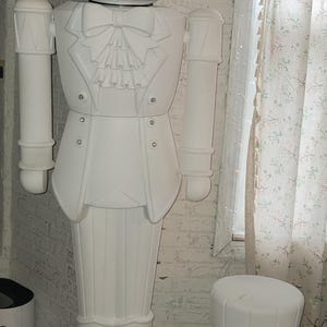 Puede incluir: Una gran estatua blanca y caprichosa de una figura parecida a un conejo con esmoquin y sombrero de copa. La estatua tiene una cara sonriente y está acompañada de una figura más pequeña con forma de calabaza con sombrero de copa. Figuras decorativas.