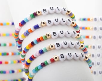 May include: A set of five elastic bracelets featuring multicolored glass beads, metallic gold spacer beads, and white round beads with the black printed text BULK. The bracelets are arranged in a stack, showcasing a vibrant array of colors.