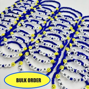 May include: A collection of blue beaded bracelets featuring white letter beads spelling ENG DF 26, interspersed with yellow smiley face beads. A yellow oval graphic at the bottom contains the black text BULK ORDER.
