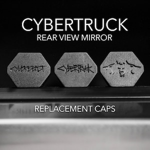 May include: Three replacement caps for a Tesla Cybertruck rear view mirror. The caps are hexagonal and made of a textured gray material. One cap features the word "Cybertruck" in a stylized font, another has the word "Cybertruck" in a different stylized font, and the third cap has a wolf head graphic.