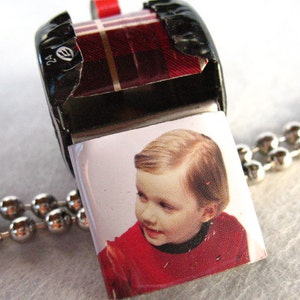 May include: A silver chain necklace with a whistle pendant. The whistle is made from a repurposed metal can and features a small photo of a child wearing a red shirt.