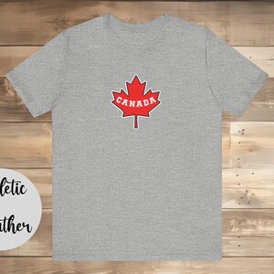 May include: A heather grey athletic t-shirt with a red maple leaf design and the word "CANADA" in white lettering.