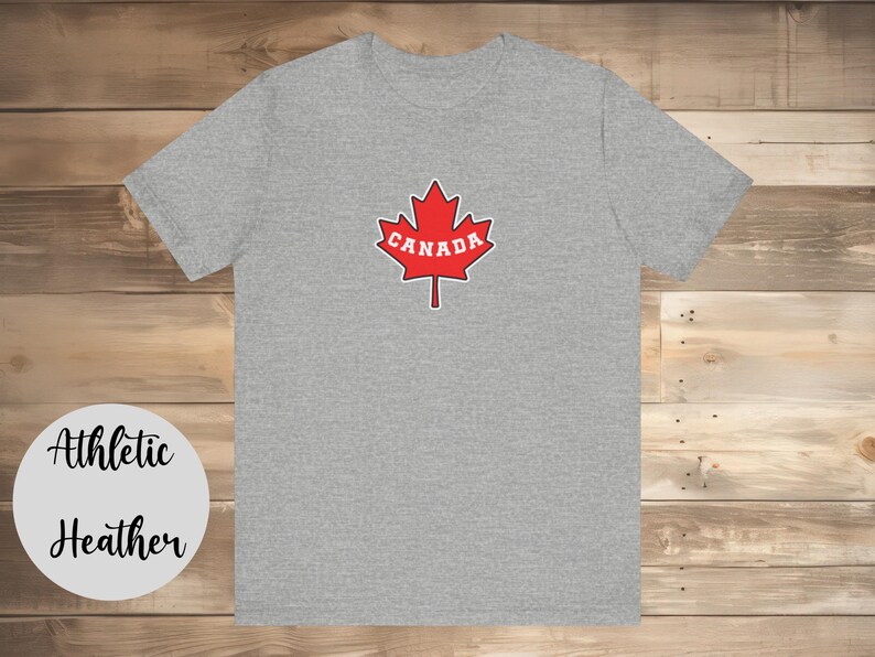 May include: A heather grey athletic t-shirt with a red maple leaf design and the word "CANADA" in white lettering.