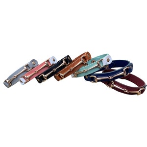 Puede incluir: Una colección de pulseras de cuero de varios colores, incluyendo gris, rosa, negro, marrón, verde azulado, blanco, azul marino y burdeos. Cada pulsera tiene un cierre de metal dorado. Accesorio de moda.