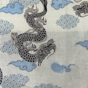 May include: A white fabric with a repeating pattern of a black and grey dragon, blue clouds, and a geometric design. The dragon is curled up and has a detailed design.