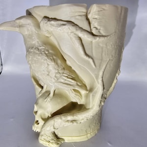 May include: A white ceramic vase shaped like a raven perched on a skull. The raven's wings are spread out and the skull is detailed with teeth and eye sockets.