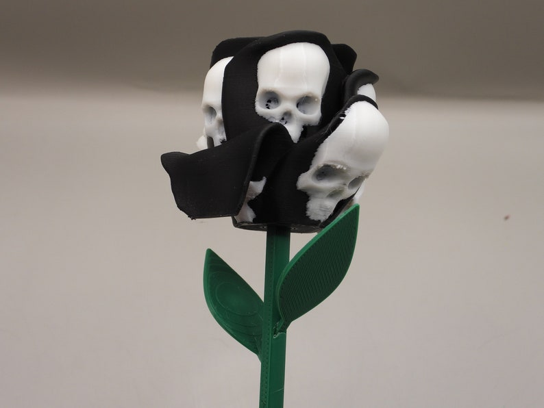 May include: A black rose with white skull details, the rose is on a green stem with two leaves.