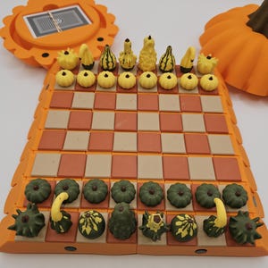 May include: A pumpkin-themed chess set with an orange and tan board. The chess pieces are shaped like pumpkins in green and yellow. The set includes a storage compartment and a decorative pumpkin.