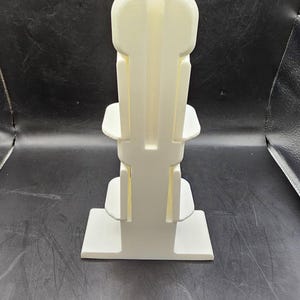 May include: White plastic tiered stand with three levels. The stand is designed to hold small items, such as jewelry or other trinkets.