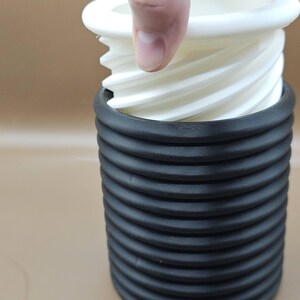 May include: A white plastic gear mechanism fits inside a black, ribbed, cylindrical container.